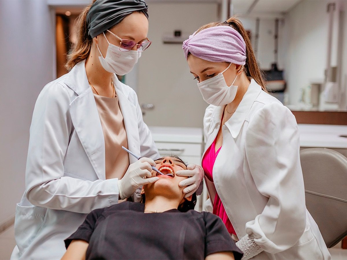 Duas profissionais da Miers Odontologia realizando atendimento a uma paciente na cadeira